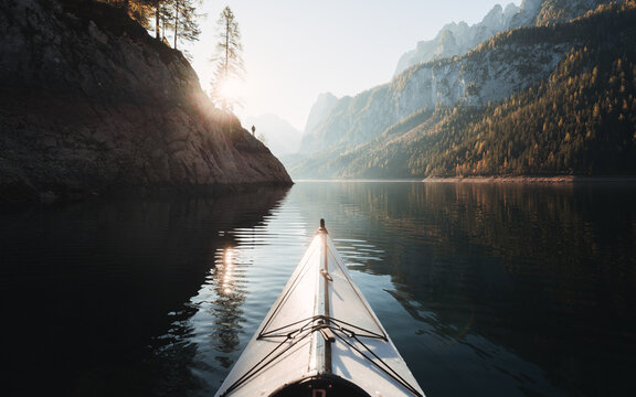 Kayaking on Gosausee lake with person standing one rocks against Dachstein mountain in the background at sunrise, Gosau, Salzkammergut region, Upper Austria, Austria	