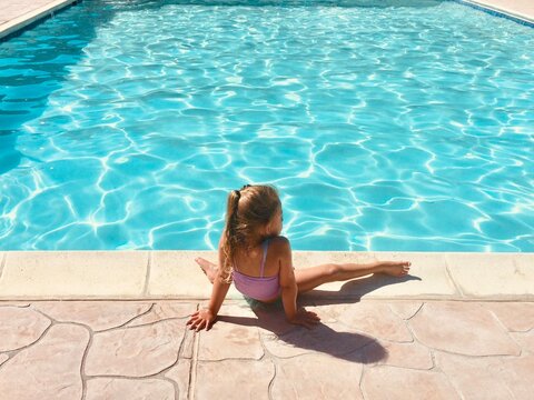 Rear view of a girl in a swimming costume sitting at the edge of a swimming pool