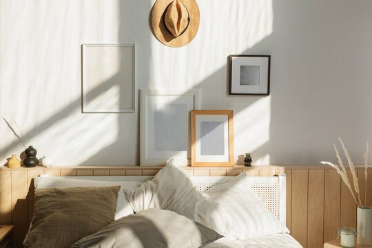 Cosy sunlit bedroom with natural shadows on a collection of assorted blank picture frames hanging over a double bed