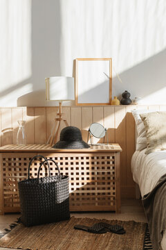 Cosy sunlit bedroom with natural shadows on a double bed, blanket box, blank picture frame and assorted personal accessories