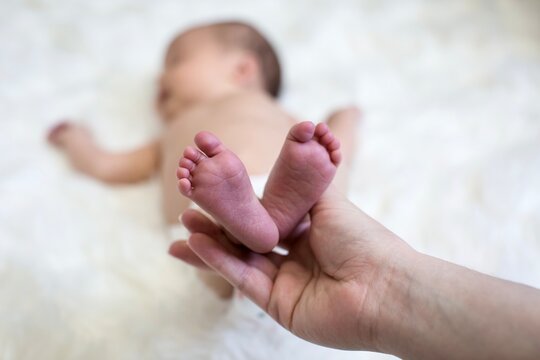 Close-up of a woman's hand holding her newborn baby daughter feet