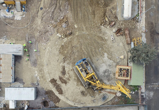 Aerial view of a large yellow drilling rig operating on a circular construction site with workers in high-visibility vests and site containers Beylikduzu, Istanbul, Turkiye.