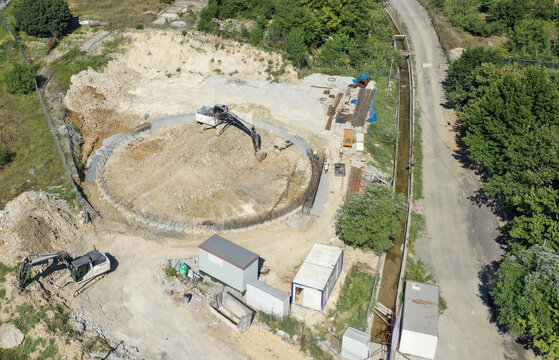 Aerial view of excavators working on a circular foundation at a construction site with workers and containers in Beylikduzu, Istanbul, Turkiye.