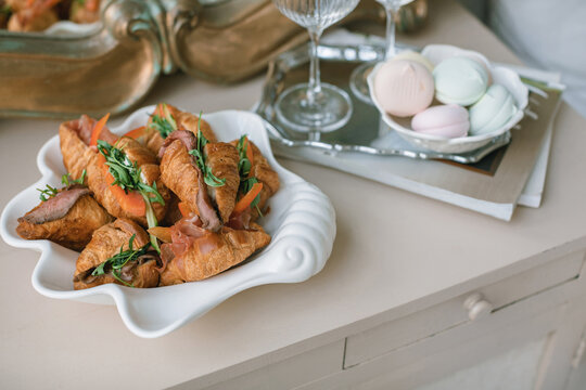 Close-up of gourmet croissant sandwiches filled with roast beef, tomato and rocket on a table next to a dish with fresh meringues
