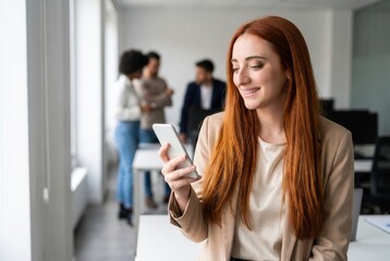 Obraz premium Smiling businesswoman using smartphone, standing in office with colleagues in background