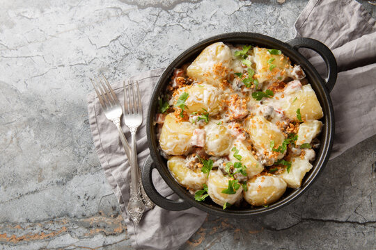 Delicious young potatoes in a creamy mushroom sauce with bacon sprinkled with breadcrumbs and parsley close-up in a frying pan on the table. Horizontal top view from above