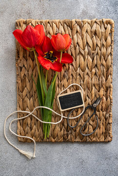 Overhead view of a red tulips on a woven place mat with a blank chalk board, scissors and string
