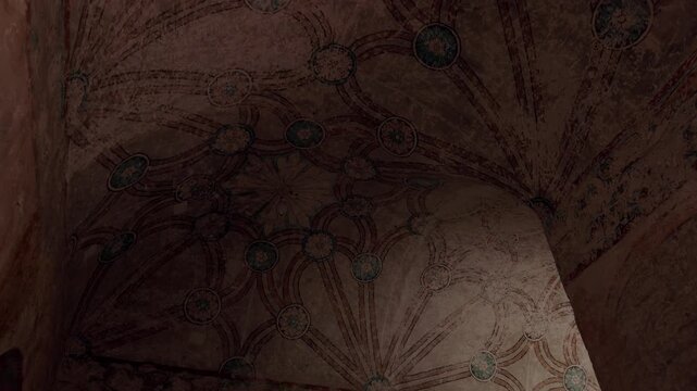Upward view of historic painted ceiling featuring decorative floral patterns and aged artistic details inside ancient architectural interior