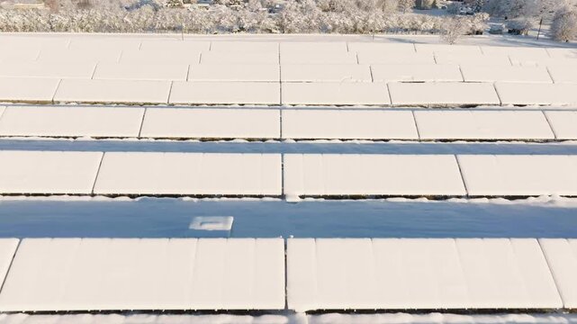 Aerial pull back of solar panel field covered in heavy winter snow, sunny day