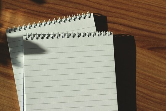 Close-up overhead view of two Blank lined spiral note pads on a wooden desk in sunlight