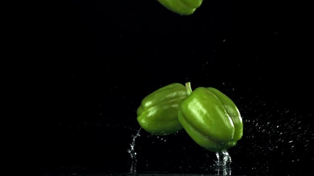 Green mini peppers tumbling on black background with slowmotion bounce Filmed on a high-speed camera at 1000 fps.