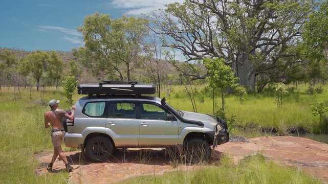 Man Folding Down Rooftop Tent On 4WD SUV Parked In Australian Outback Savanna, Ground Level Shot