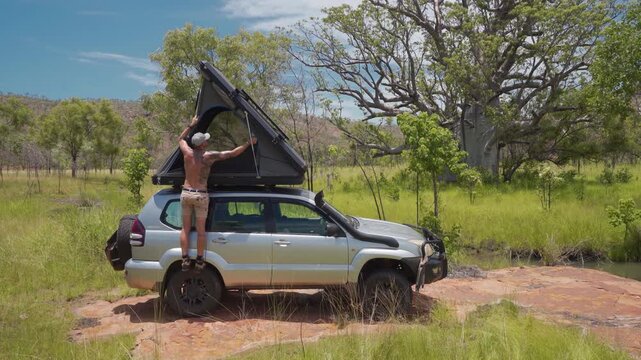 Man Closing Rooftop Tent On 4WD Toyota Prado In Australian Outback Savanna, Ground Level Shot