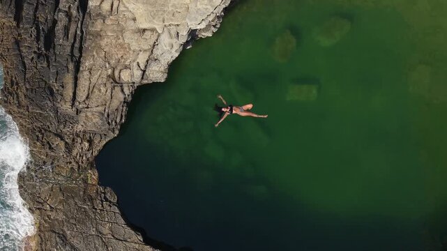 Vertical drone shot of a woman swimming in the turquoise Giola natural pool in Thassos, highlighting rocky formations and crystal clear water.
