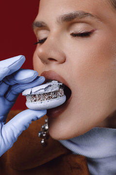 Close-up of a stylish woman wearing gloves savouring a lavender macaron