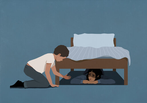 Brother reaching out to comfort scared sister hiding underneath bed at bedtime