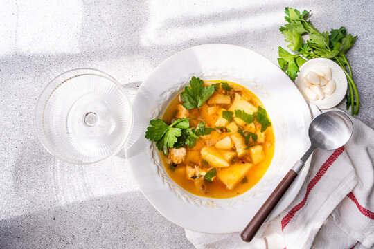 Close-up overhead view of a bowl of Healthy chicken soup with potatoes, carrots, parsley and fresh garlic cloves on a table with a wine glass and tea towel