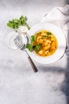 Close-up overhead view of a bowl of Healthy chicken soup with potatoes, carrots, parsley and fresh garlic cloves on a table with a wine glass and tea towel
