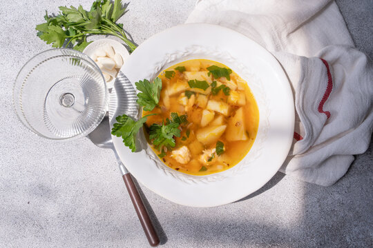 Close-up overhead view of a bowl of Healthy chicken soup with potatoes, carrots, parsley and fresh garlic cloves on a table with a wine glass and tea towel