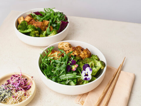 Fresh, healthy salads in bowls with edible flowers next to chopsticks
