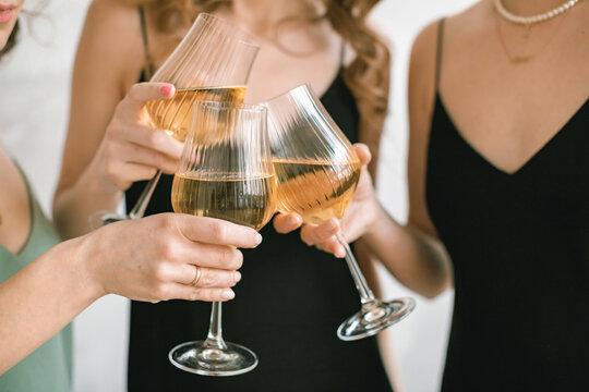Close-up of three women in party dresses making a celebratory toast with glasses of white wine