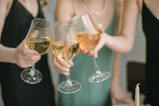 Close-up of three women in party dresses making a celebratory toast with glasses of white wine