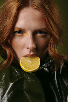 Close-up portrait of a woman with long red hair eating a slice of lemon