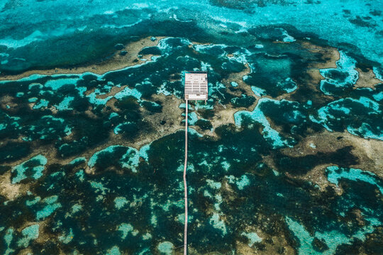 Aerial view of a wooden pier leading to a platform over a vibrant coral reef in the turquoise ocean near Kudahuvadhoo, Dhaalu Atoll, Maldives.