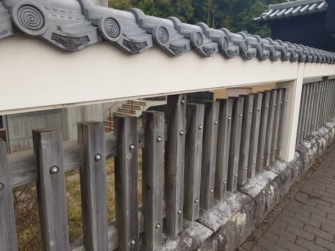 Traditional Japanese roof tiles and wooden fence on a white wall