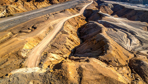 Aerial view of a dry arid landscape with winding dirt roads and eroded gullies, geological formations and arid terrain, resource extraction or mining site