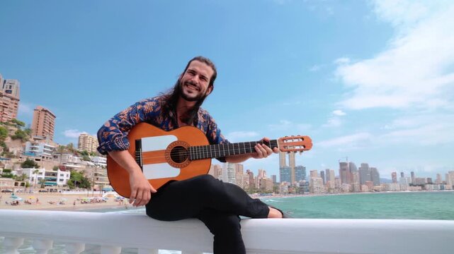 Dolly in shot of happy Spanish flamenco guitarist looking at camera, sea background