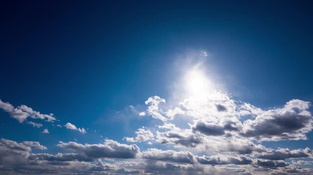 White fluffy clouds drift rapidly across a deep blue sky as the bright sun shines from above. This time-lapse captures the fast-moving weather patterns and changing light during a clear day.