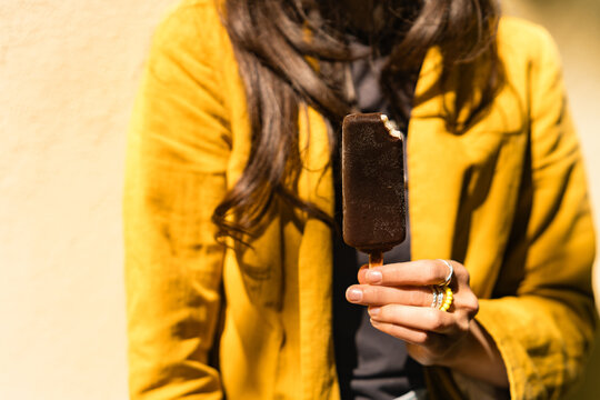 Close-up of a woman standing outdoors on a sunny day eating a chocolate ice cream lolly