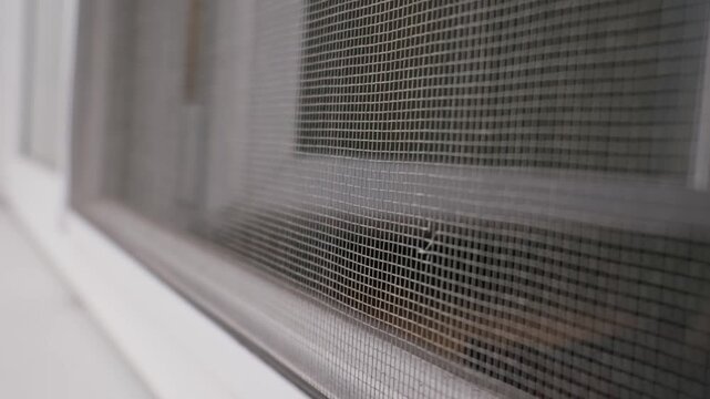 Close-up of woven grey mesh mosquito net on a white plastic window frame. Concept of insect protection, home improvement, and safe residential indoor spaces.