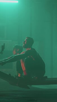 Athletes performing functional training using rowing machines in an indoor gym environment focused on strength, endurance, and full-body workout in low light conditions