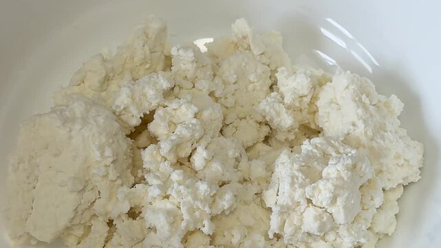 Natural cottage cheese served in white plate with delicate grainy texture and fresh homemade dairy atmosphere for healthy breakfast or dessert preparation.
