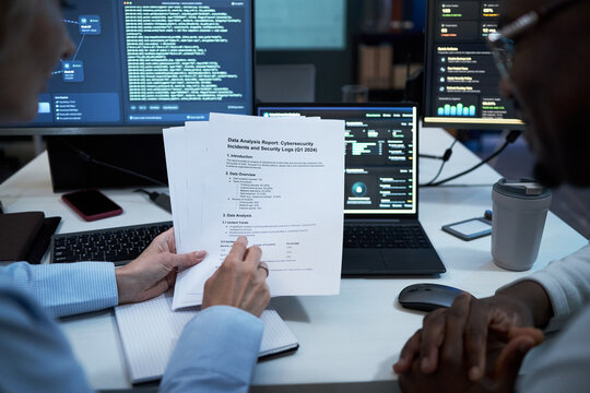Close up of coworkers reviewing cybersecurity incident report and security logs beside coding dashboard, discussing risk analysis and compliance. For IT audit, data breach response, corporate security