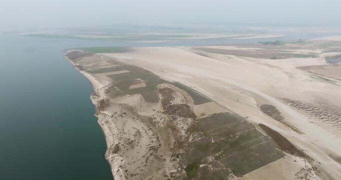 Aerial view of the vast river landscape with sandy banks, agricultural fields, and calm water under a hazy sky in Kurigram, Rangpur Division, Bangladesh.