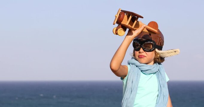 Happy child playing with toy wooden airplane at the beach during summer vacation. Slow motion