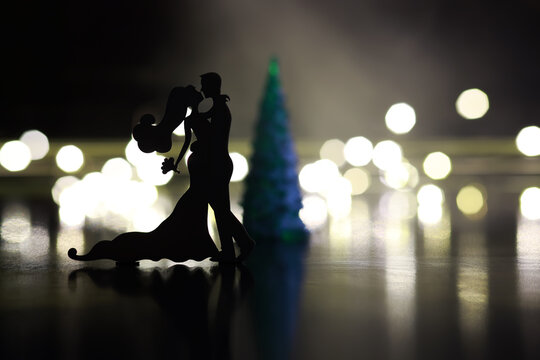 Black silhouettes of pair dancers performing. Man and woman are dancing on gray background with white backlight. Choreography. New Year's ball