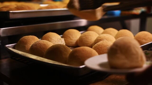 freshly baked Filipino bread called Pandesal being picked up by a tong and placed on a plate.