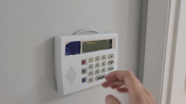 Close up video footage of a person pressing buttons on a residential home security alarm keypad mounted on a wall. Modern electronic security system control panel with numeric code entry for home prot