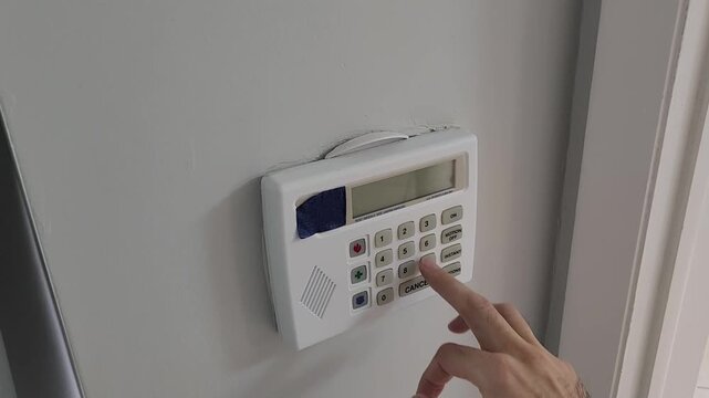 Video footage of a hand pressing buttons on a wall mounted electronic security keypad inside a modern home. Residential alarm system used for access control, authentication and property protection.
