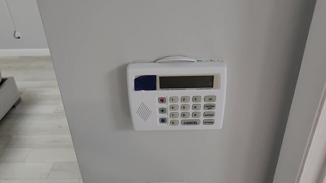 Person using wall mounted security alarm keypad inside modern home