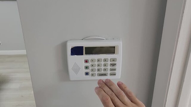 Close up video clip of a person shielding the keypad while typing a passcode into a residential security alarm control panel. Home access protection and electronic authentication concept.