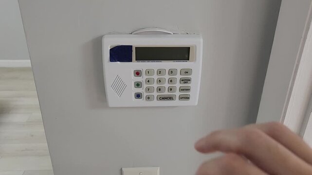 Finger pressing blue function button on residential security alarm keypad