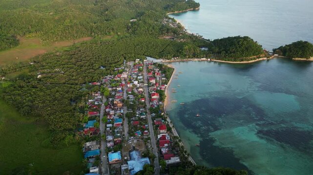 Scenic aerial orbit of Magnesia Del Norte in Virac, Catanduanes with coastal village, clear bay, and lush tropical hills
