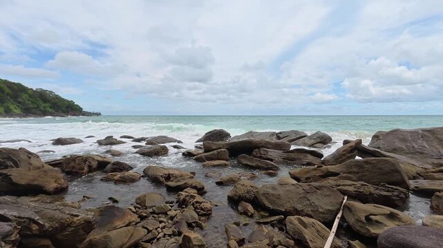 Waves crash over smooth rocks in a tropical coastal setting.