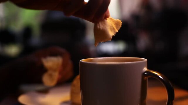 Hand breaking of a piece of Filipino bread called Pandesal and dipping it into a mug of coffee.