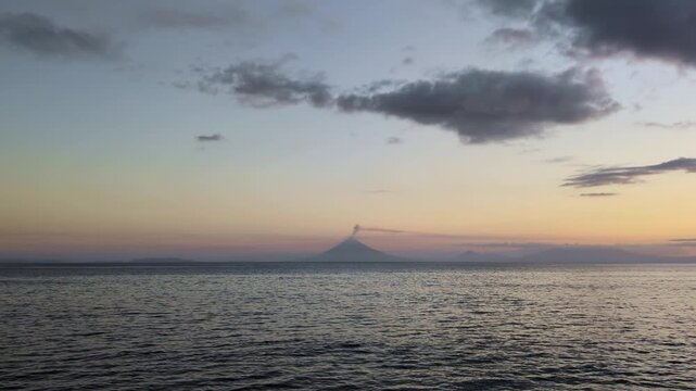 Wide static shot of the Bicol seascape at sunset with calm water, distant island silhouette, soft clouds, and a glowing horizon - Luzon, Philippines